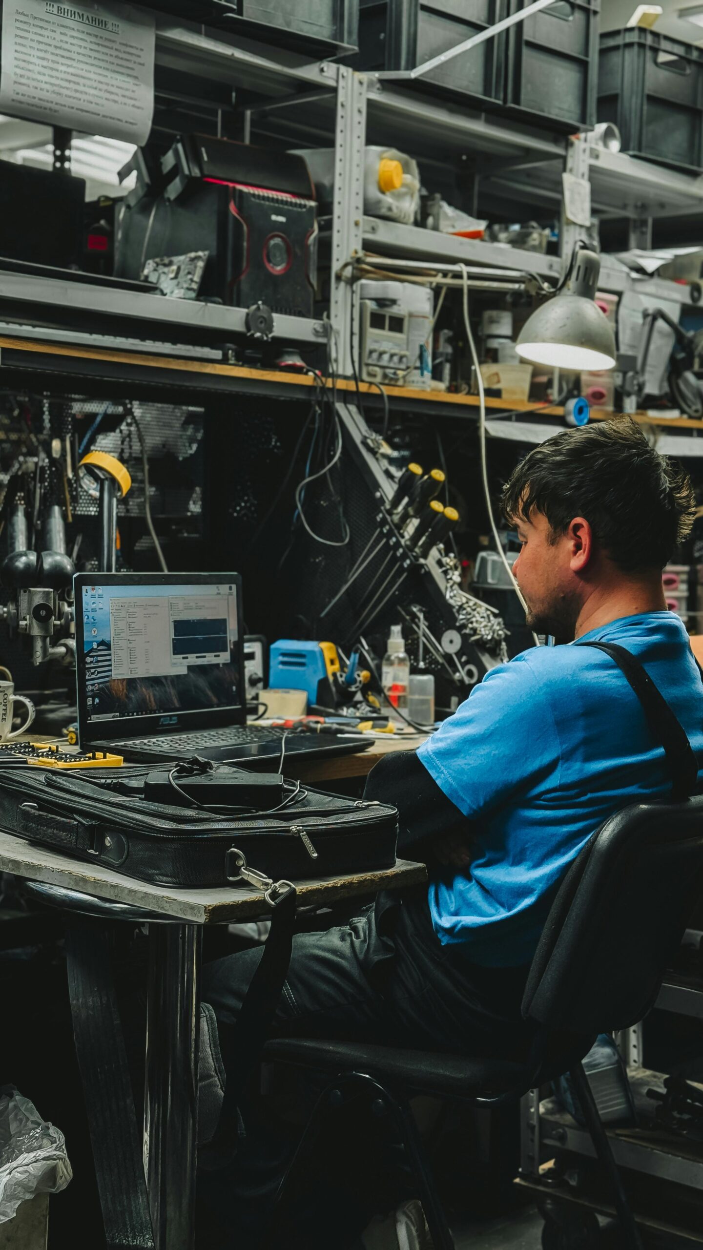 Engineer focused on laptop in cluttered workshop. Ideal for tech and industry themes.